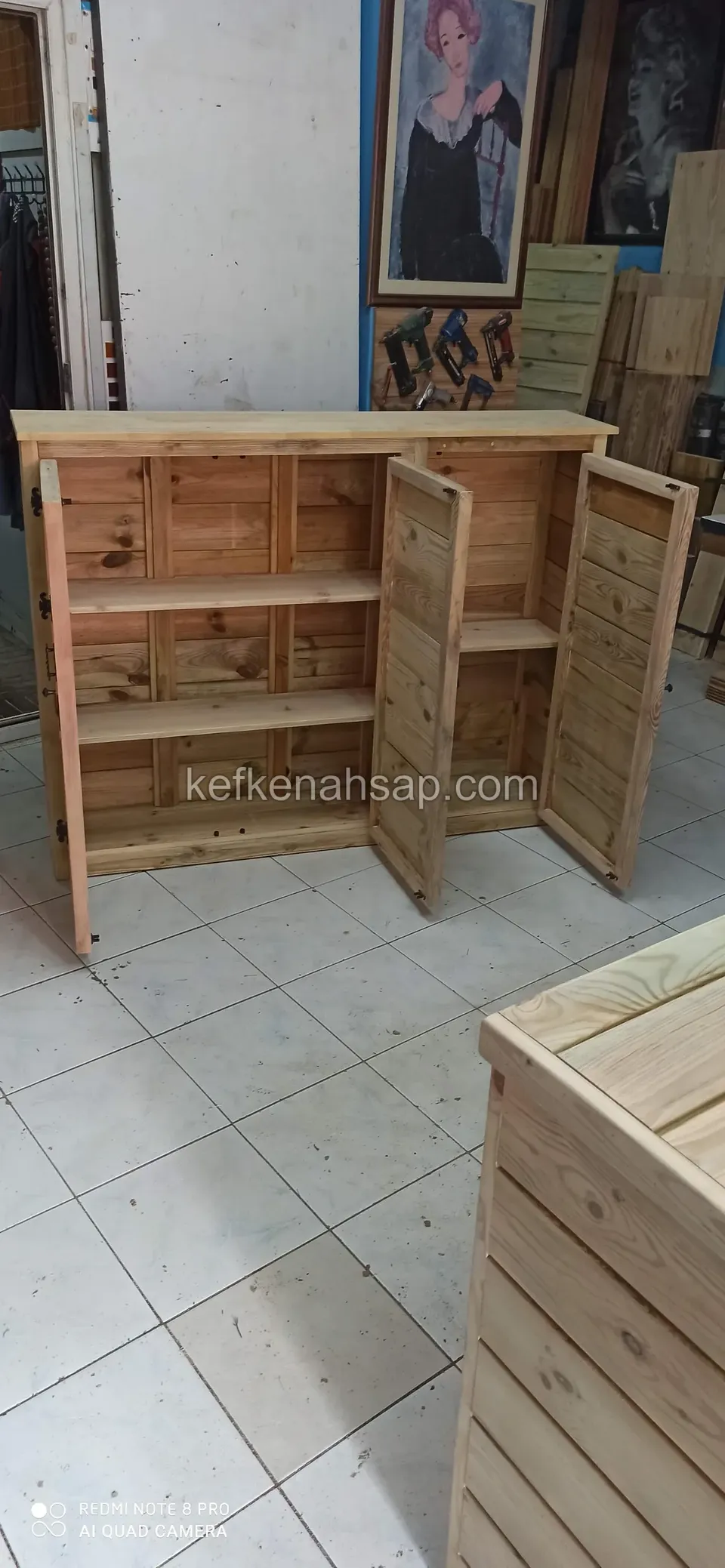 Ein Holzschrank mit offenen Türen und Einlegeböden, vorn rechts ein weiterer Holzkasten mit waagerechter Bretterverkleidung