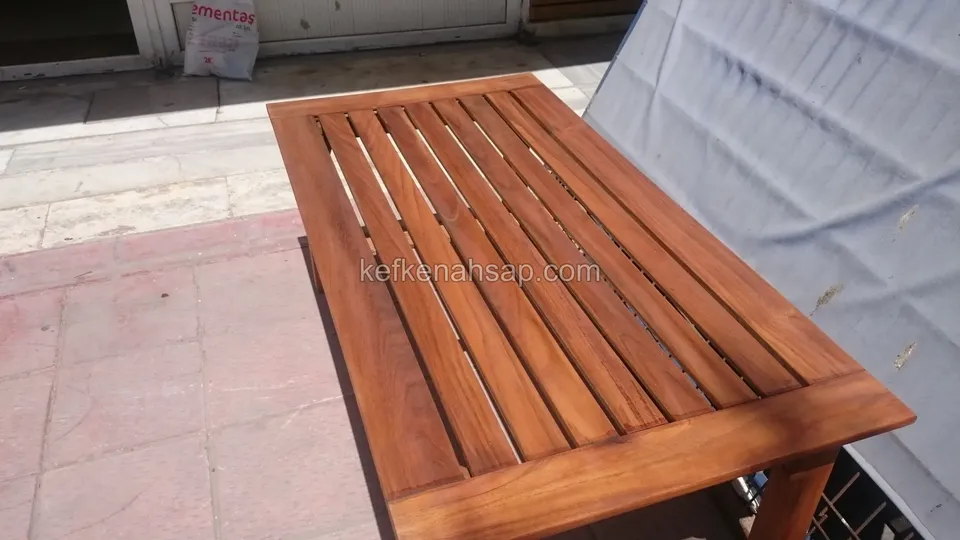 Karo zeminli teraste duran, çıtalı üstü ve geniş çerçevesi olan dikdörtgen ahşap masa