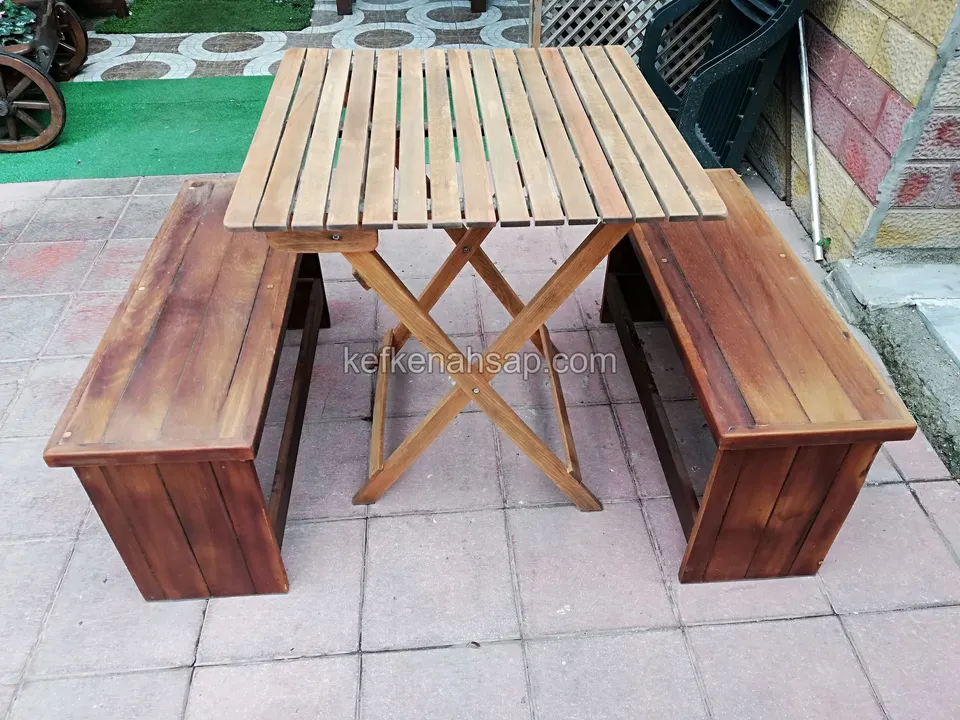 Auf Verbundpflaster steht ein Klapptisch aus Holzlatten mit je einer dunkel lackierten Holzbank an den Seiten