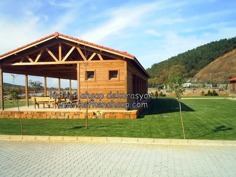 Breiter Holzpavillon mit Ziegeldach, darunter Holztische, davor Rasen und Pflaster