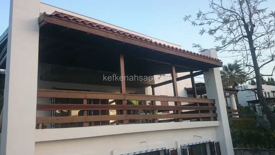 Kiremit çatılı geniş terasın yatay çıtalı ahşap korkuluğu; yanda palmiye ve çıplak ağaç