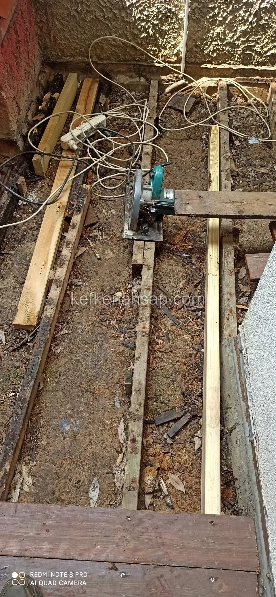 A circular saw and tangled power cables between long joists in a narrow strip of soil