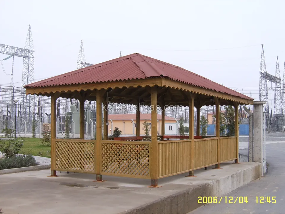 Kırmızı çatılı uzun dikdörtgen kamelya, kafes panelli alçak duvarlar, arkada elektrik direkleri ve yol