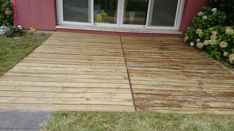 Deck on a lawn in front of the glass doors of a red-walled house, with its right half darker and more stained than the left