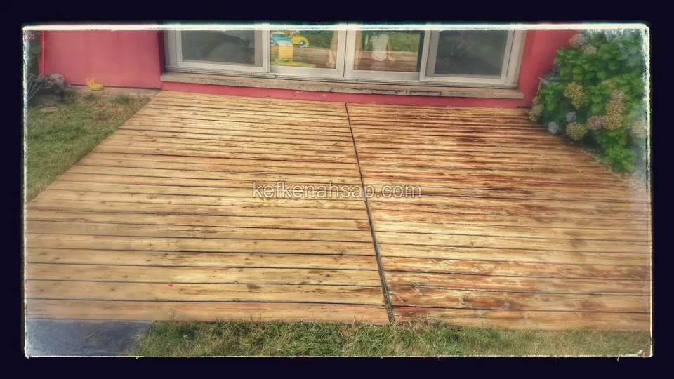 Stained, faded light brown deck on a lawn in front of the windows of a red-walled house