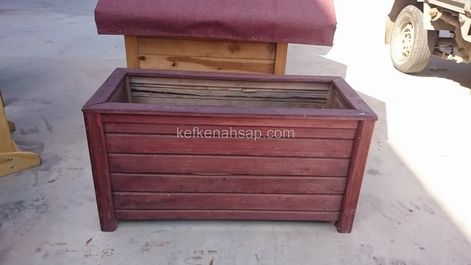 Kırmızımsı vernikli yatay çıtalı uzun ahşap sandık biçiminde çiçeklik; arkada kapaklı başka bir ahşap kutu