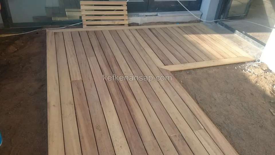 Partly laid timber deck with an L-shaped notch, with a pallet and soil behind