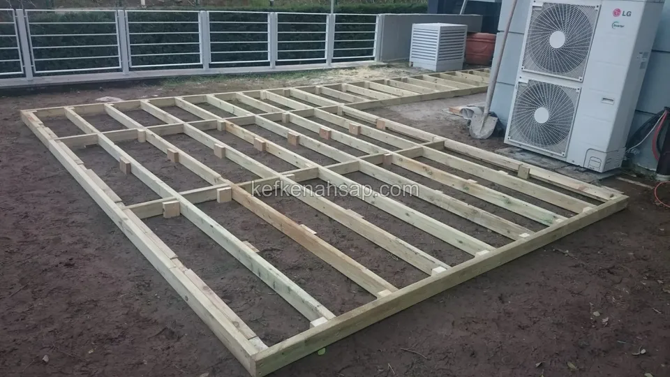 Timber deck substructure on soil beside an outdoor air-conditioning unit, with a metal railing behind