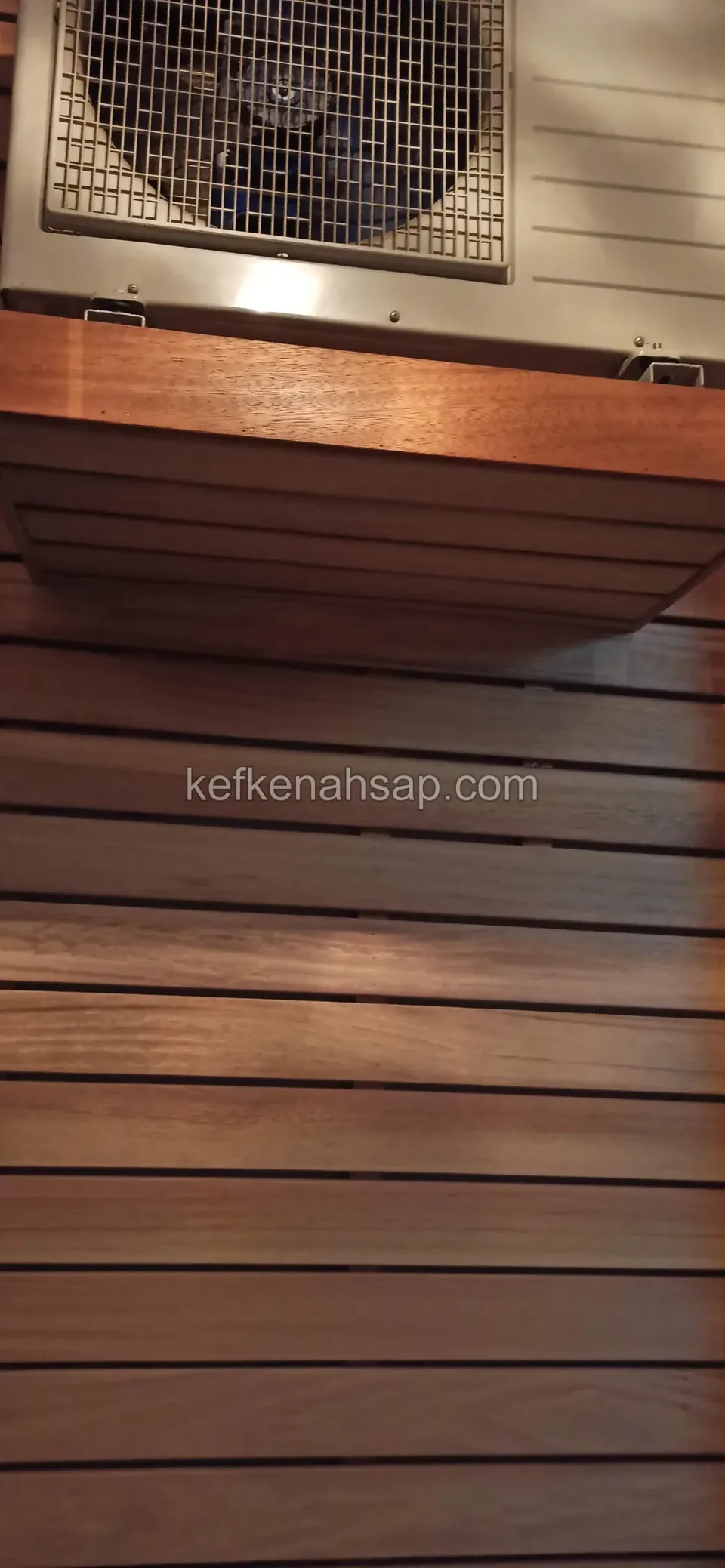 Reddish-brown slatted timber housing below an air-conditioner outdoor unit with a hinged lid and a metal catch at its end