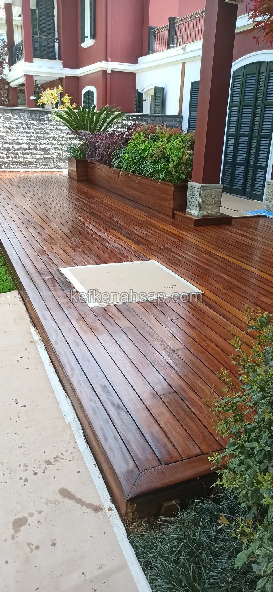 Timber planter full of plants beside a red-painted column, with a dark brown polished deck in front