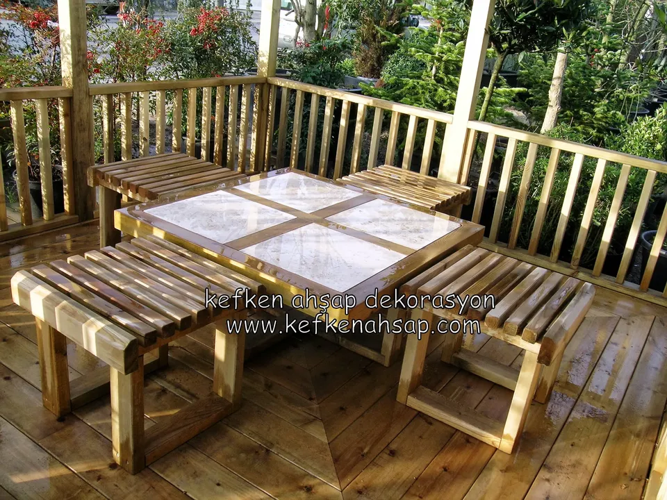 On a timber deck fenced by slatted railings, a low table with ceramic tiles inset and two slatted stools