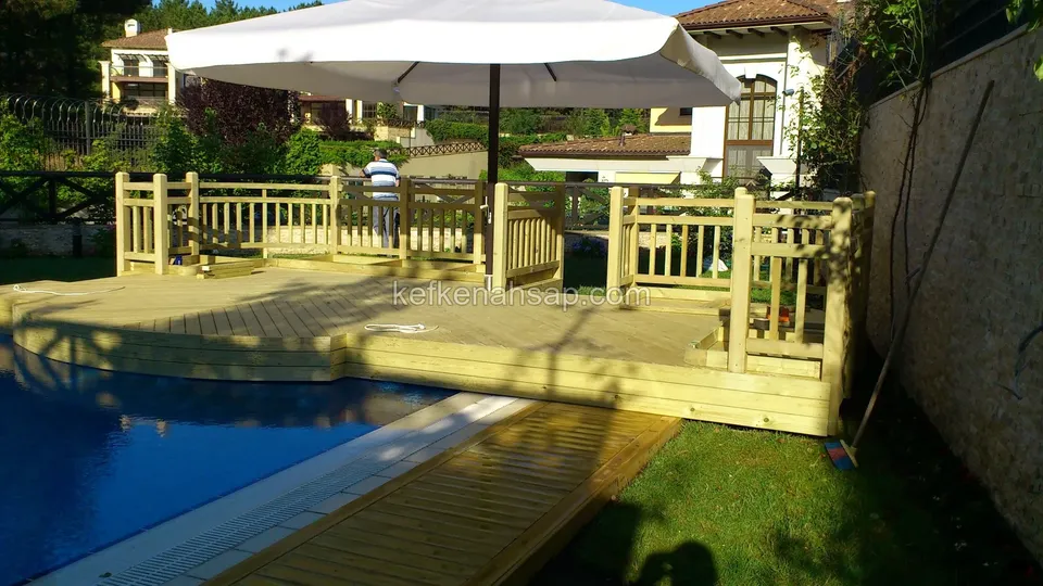 Platform with a vertical-slat timber railing at the pool edge, with a narrow deck path leading to the lawn beside it