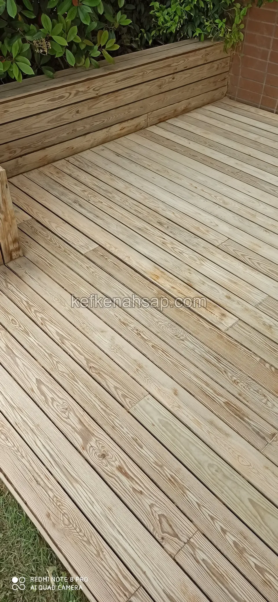 Heller unbehandelter Terrassenbelag mit einer Holzsitzbank in der Ecke an der Wand