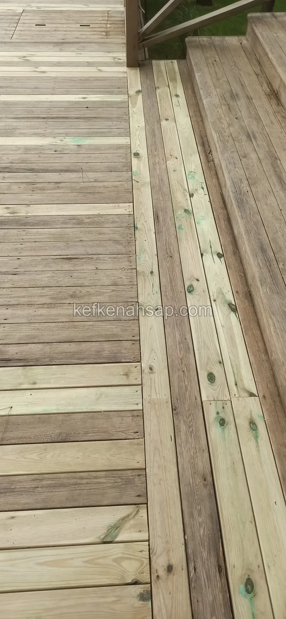 Deck on which new pale boards are mixed in with old grey ones, with a railing showing in the corner