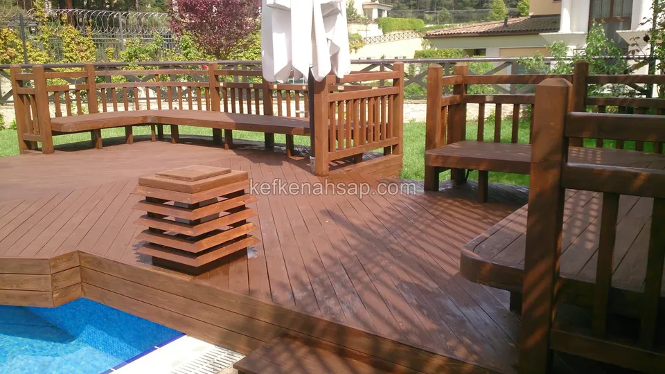 Havuz kenarında koyu kahverengi deck üzerinde köşe bank, alçak masa ve kademeli ahşap fener