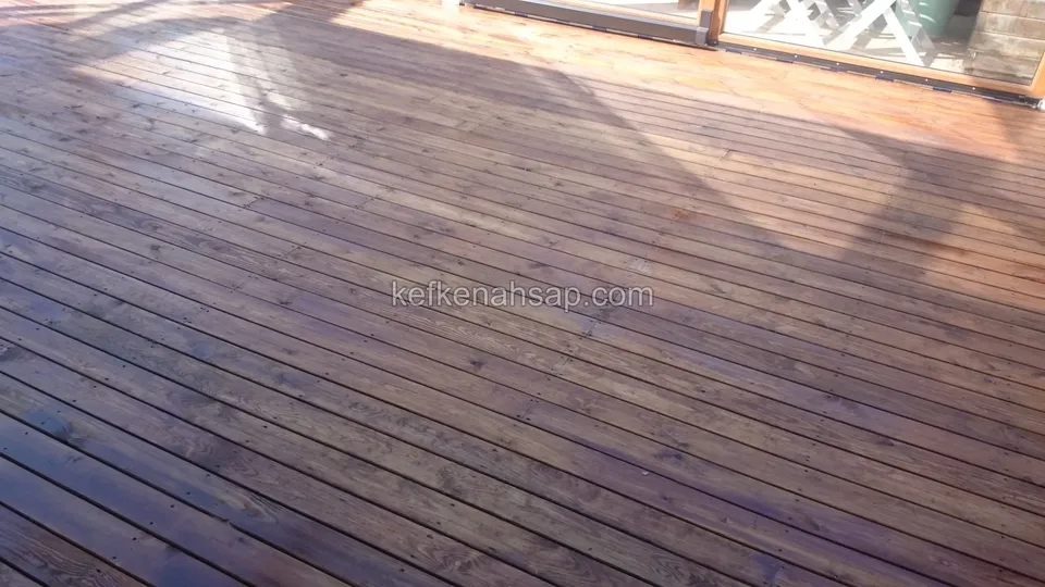 Teras girişine kadar uzanan, koyu kahve ve parlak yüzeyli ahşap deck tahtaları