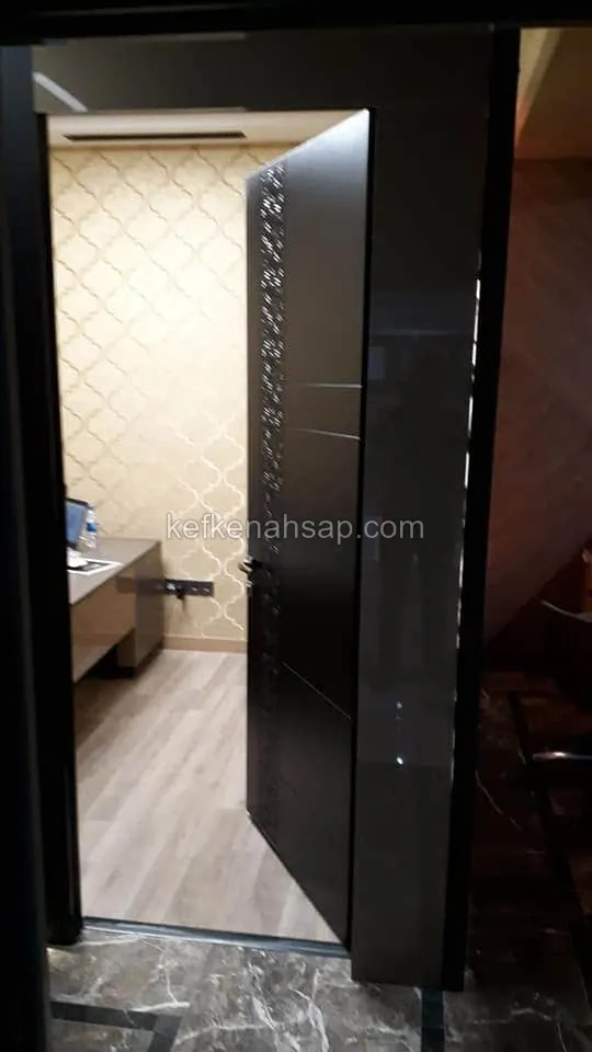 باب داكن لامع نصف مفتوح، وعلى حافته شريط عمودي بنقش منحوت، وخلفه غرفة مكتب بجدران بنقش ذهبي وطاولة