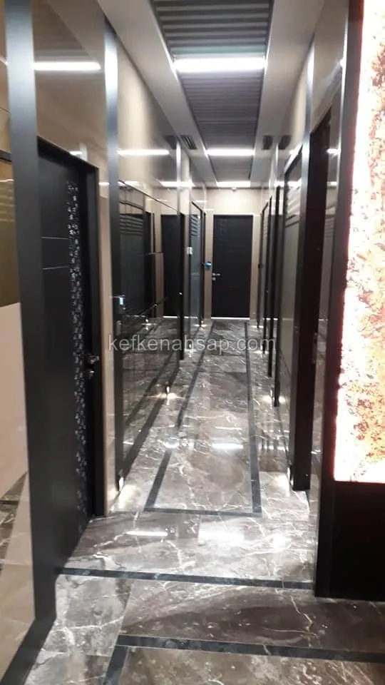 ممر طويل بأرضية رخامية وعلى جانبيه أبواب داكنة وفواصل زجاجية ولوح مضاء في السقف