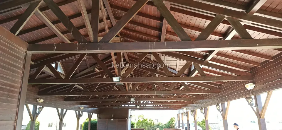 Ahşap lambri tavanlı geniş bir kamelyanın içinden görülen koyu kahve tonlu çatı makasları ve kirişler