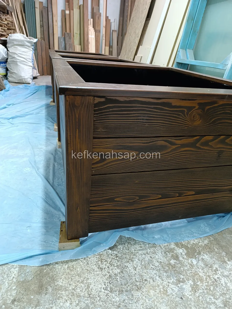 Side of a dark-varnished timber planter with the grain clear on the horizontal boards