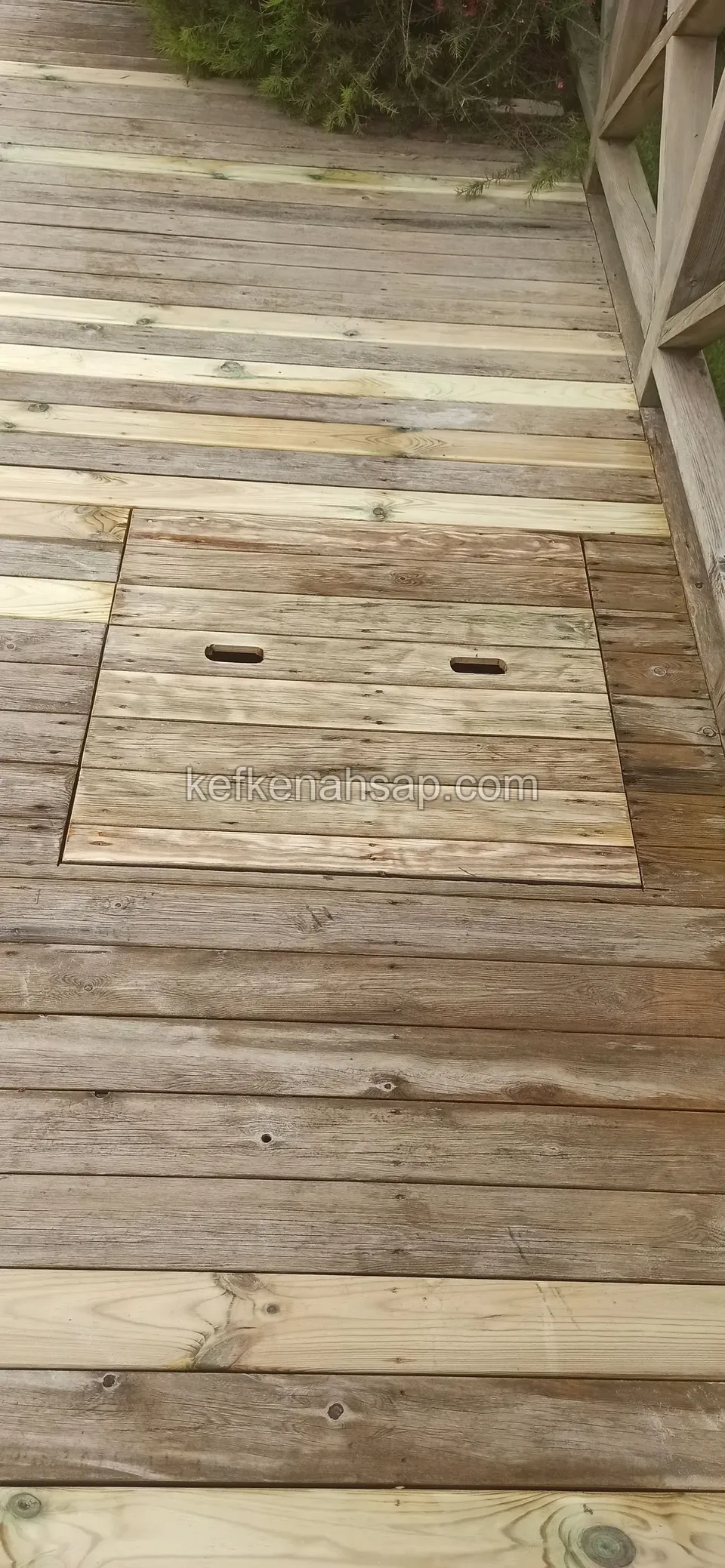 New pale boards across an old grey deck, with a hatch lifted by two finger holes in the middle