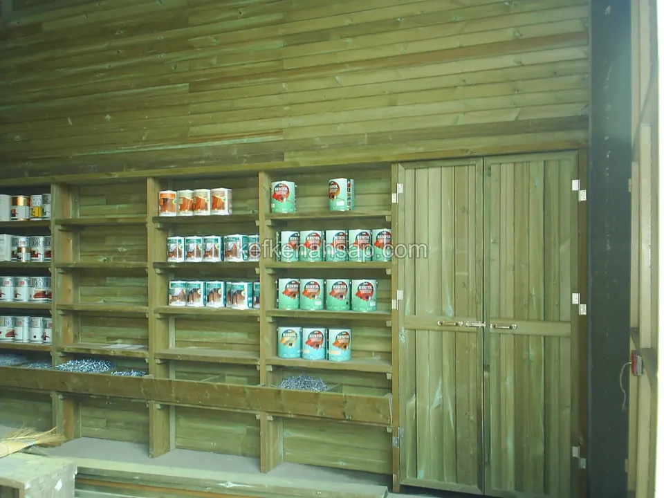 Gefächerte Holzregale in der Wand eines mit Brettern verkleideten Häuschens, daneben eine Doppeltür, in den Regalen Farbdosen