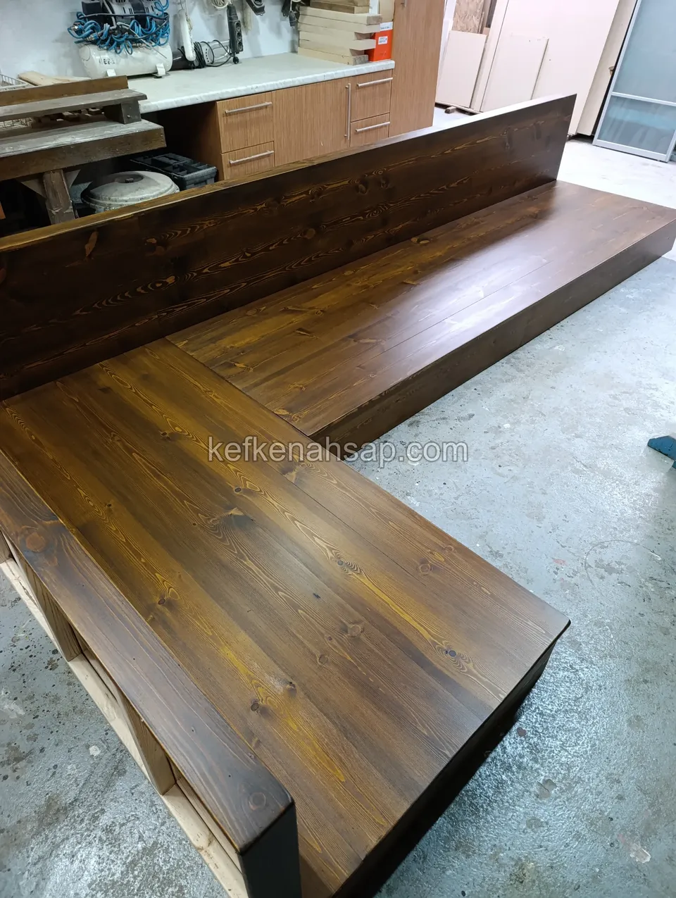 L-shaped wooden seating bench with a high backrest and wide seat, stained dark brown, standing in a workshop