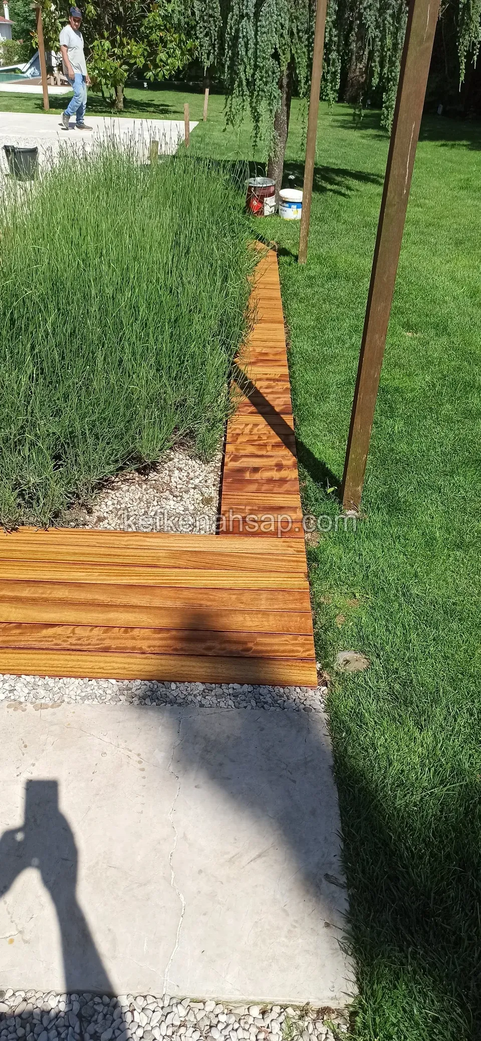 Lavanta bitkileri kenarında turuncu ahşap deck şeridi; yanda ahşap direk ve beton plakalar