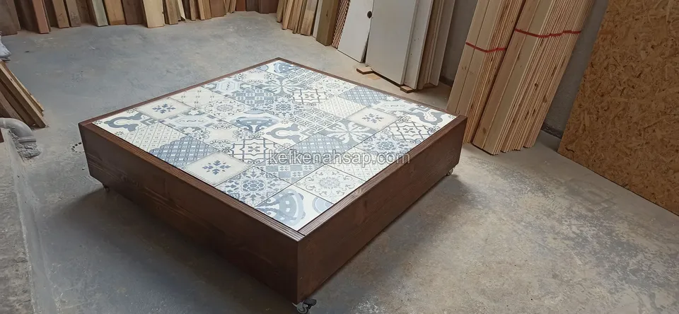 Niedriger quadratischer Tisch mit blau-weißer Keramikplatte und dunklem Holzrahmen in einer Werkstatt