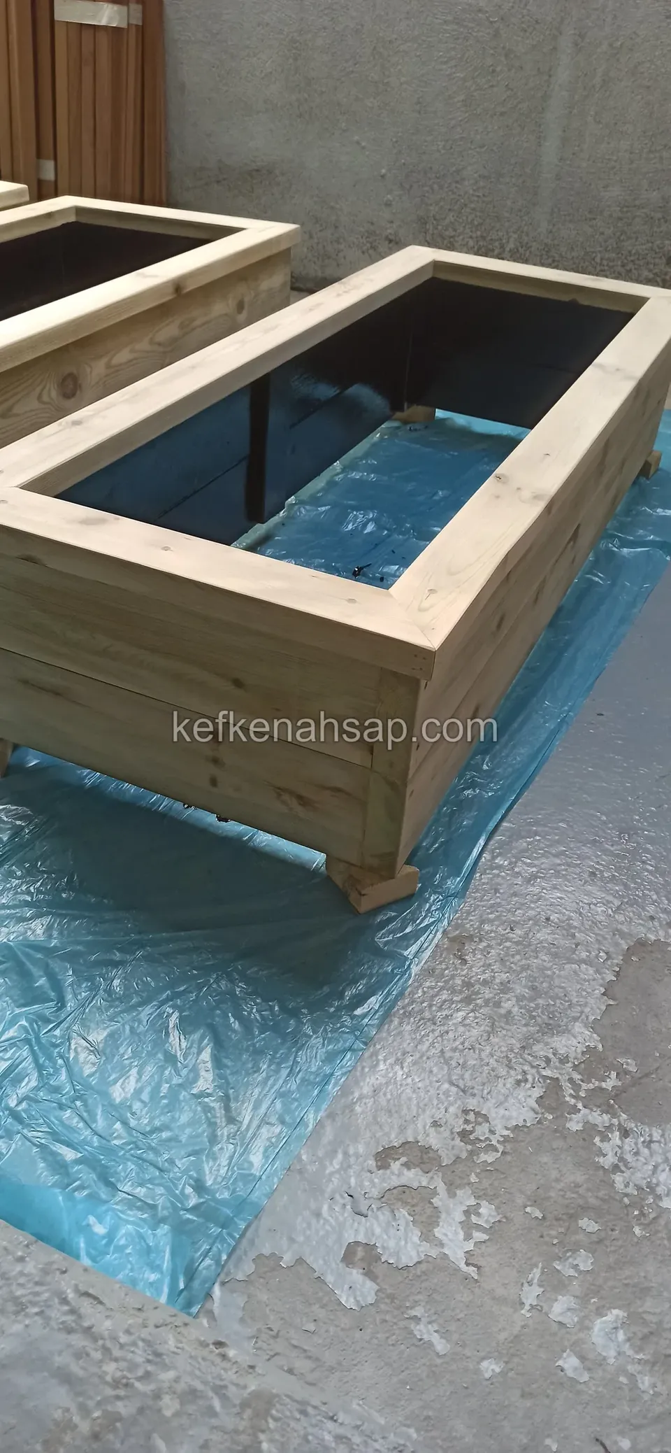 Long timber planter on short feet standing on blue plastic, with a blue-black liner inside