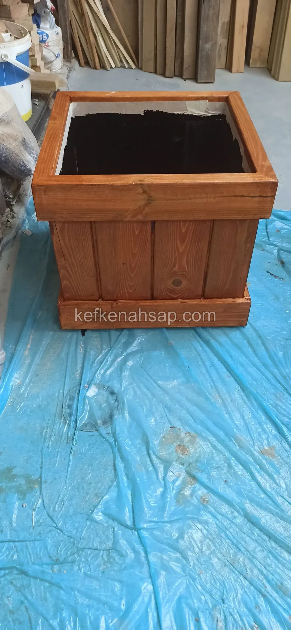 Square varnished timber planter with a black liner standing on a blue sheet
