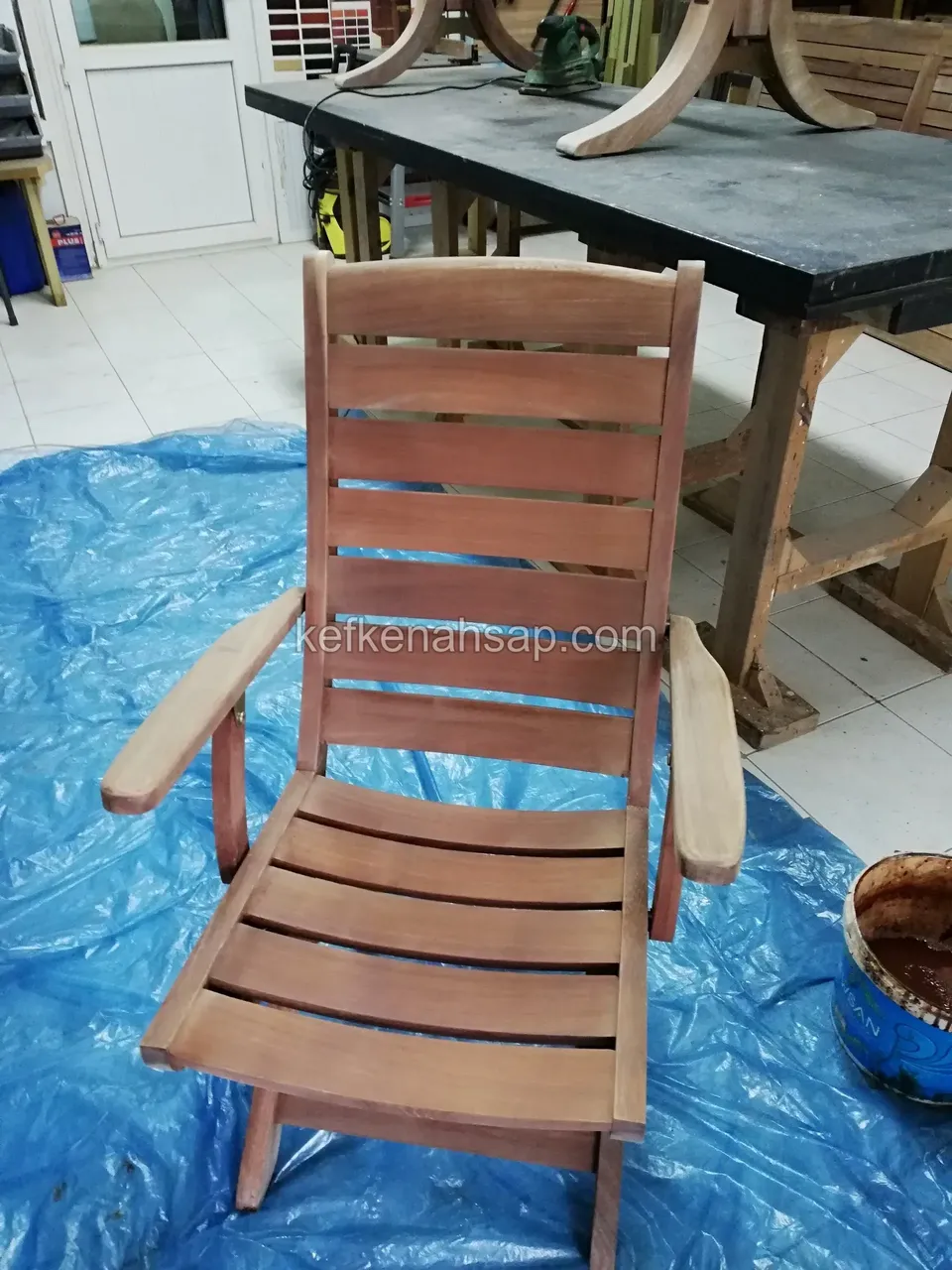 Ein Holzstuhl mit Armlehnen und breiten Latten steht auf einer blauen Plastikplane und wartet auf Lack oder Farbe
