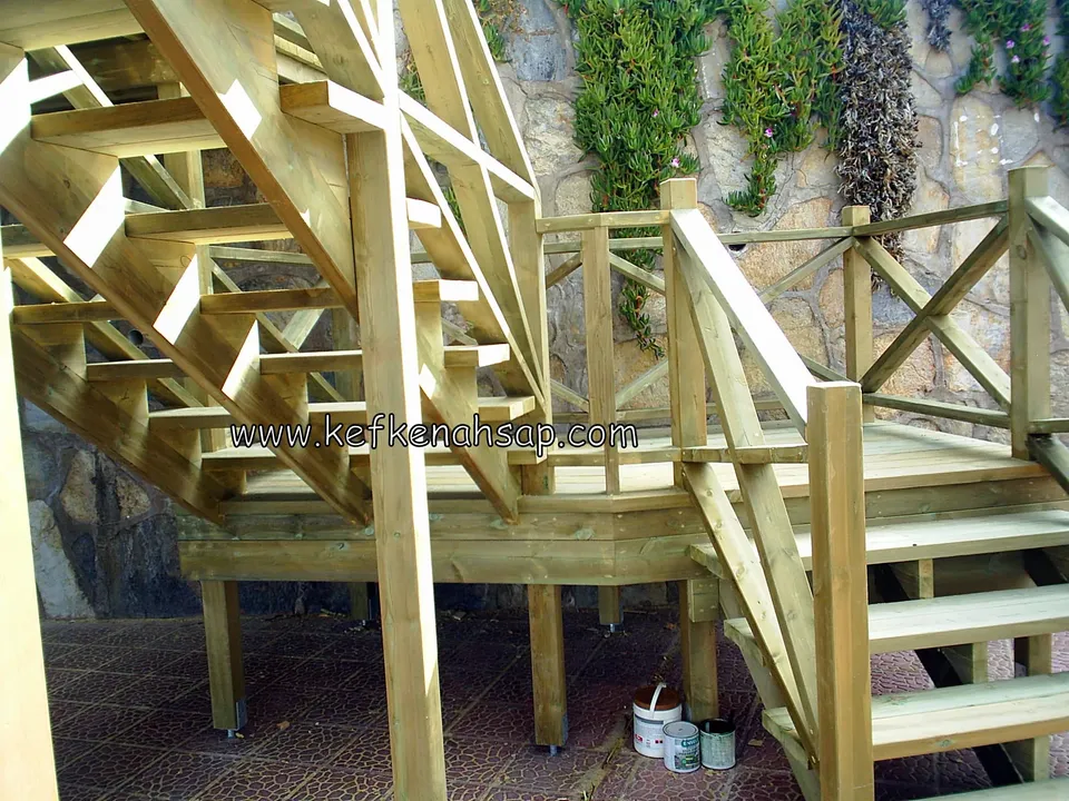 Holzpfosten und Balken in der Unterkonstruktion von Plattform und Treppe, am Boden Farbeimer, dahinter eine Steinmauer