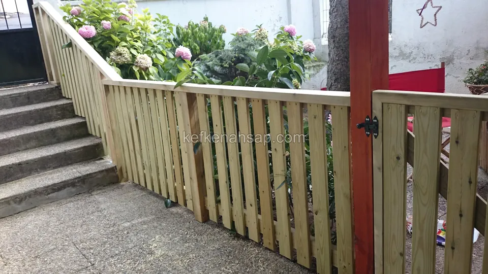 Grünliches Holzgeländer mit senkrechten Latten und ein Torflügel an schwarzen Scharnieren neben Steinstufen