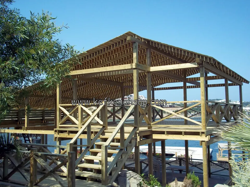 Pavillon mit Lattendach am Meer, dessen Obergeschoss mit Diagonalgeländer über eine Holztreppe erreichbar ist
