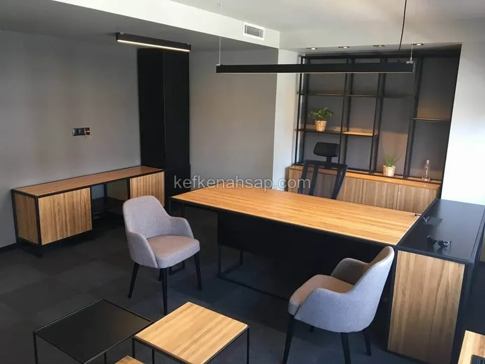 Siyah metal çerçeveli ahşap yönetici masası, gri koltuklar, kitaplık ve sehpalar bulunan koyu tonlu ofis odası