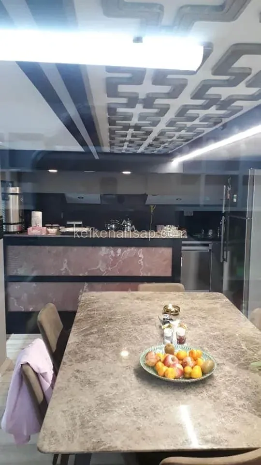 Geometrik desenli tavan kaplaması, bar tezgâhı ve taş yüzeyli yemek masası olan modern bir mutfak