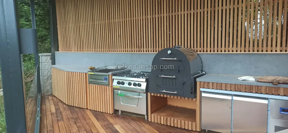 Außenküche auf einem Deck aus Holzbackofen, Herd und mit Holzlatten verkleideten Schränken