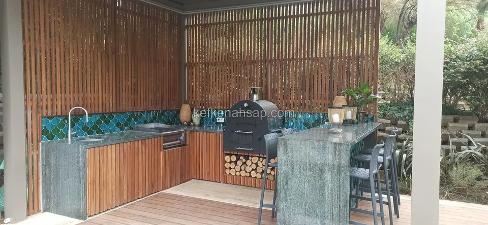 Çıtalı ahşap paravan arasında odun fırını olan dış mutfak; yanında taş bar ve tabureler