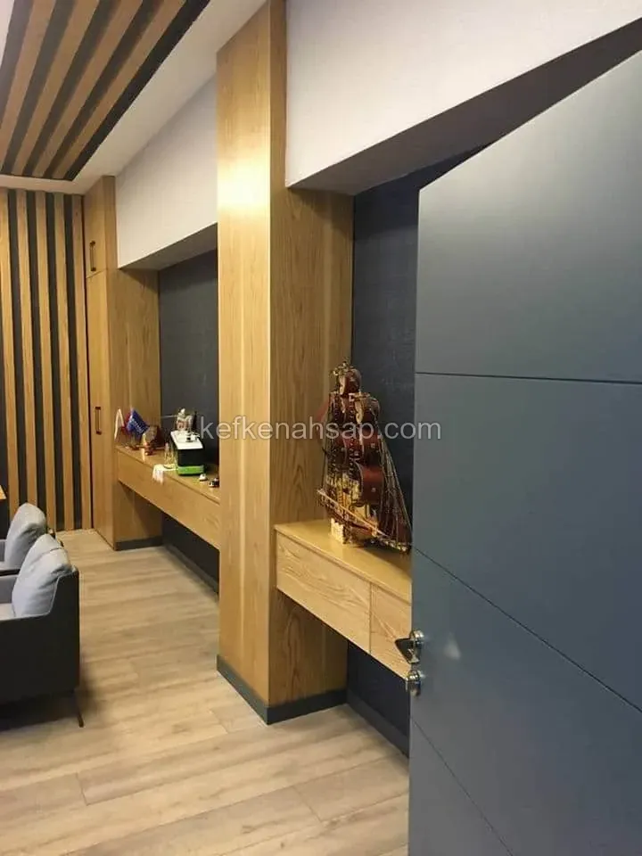 Ahşap kaplı sütun, çıtalı duvar ve tavan, yan duvarda çekmeceli açık renk konsol ile antrasit renkli kapı olan ofis odası