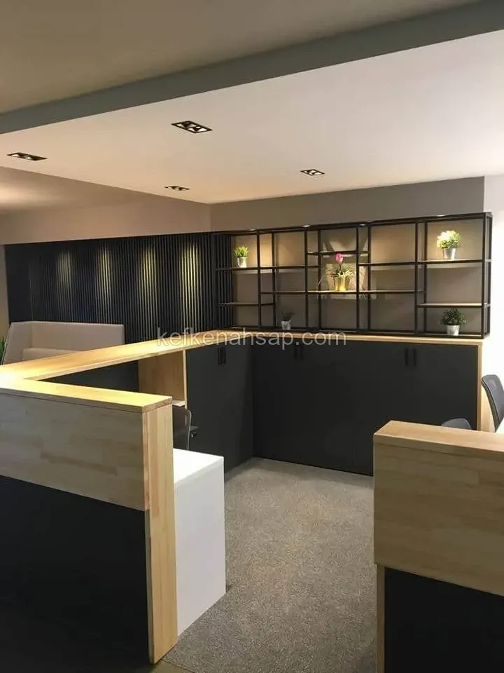 Açık renk ahşap üstlü L şekilli ofis tezgâhı, antrasit dolaplar, dikey lambri duvar ve siyah metal çerçeveli raf