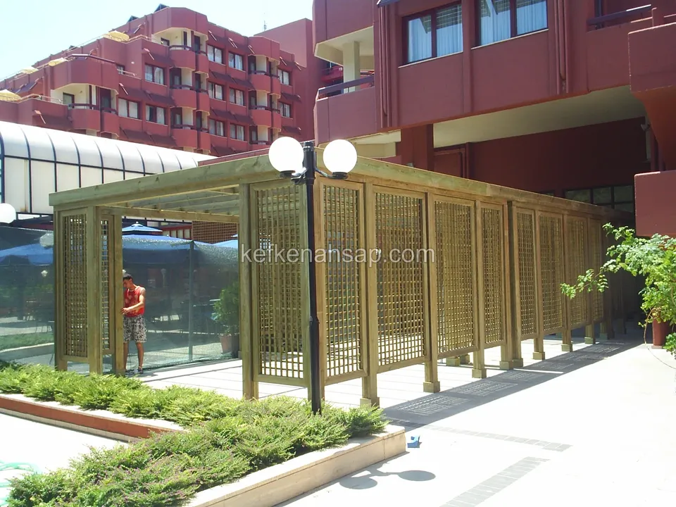 Otel girişinde kafes panelli uzun ahşap geçit pergolası, aydınlatma direği ve bitkili düzenleme