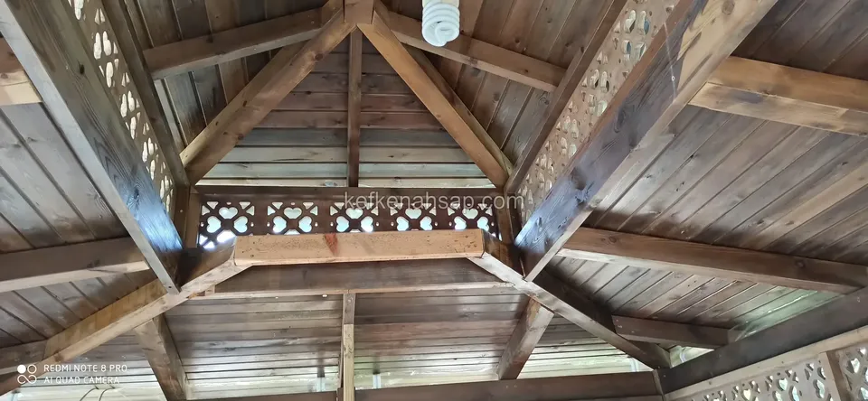 Kamelyanın koyu tonlu çatı altı, kirişler arasında oyma desenli kafes bölümler ve tahta kaplama