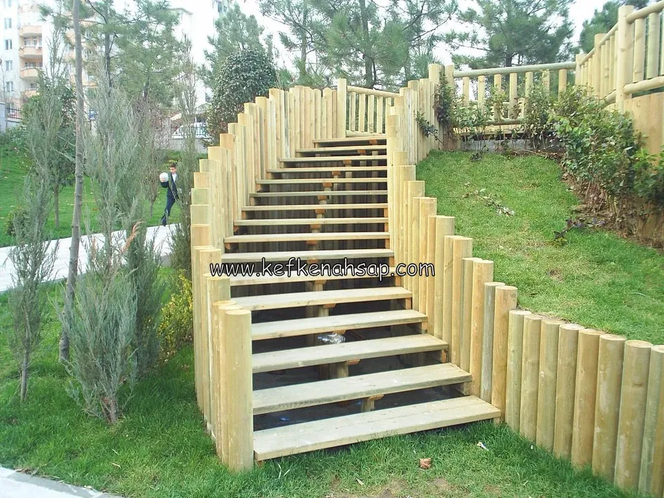Parkta eğimli arazide yuvarlak ahşap kazıklarla çevrilmiş, açık basamaklı ahşap merdiven ve çevresindeki çim alan