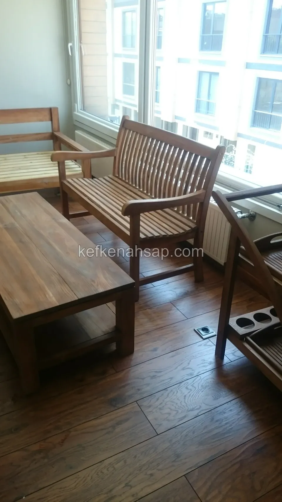 A timber bench with arms and a slatted back and a low rectangular table in a room with a dark parquet floor
