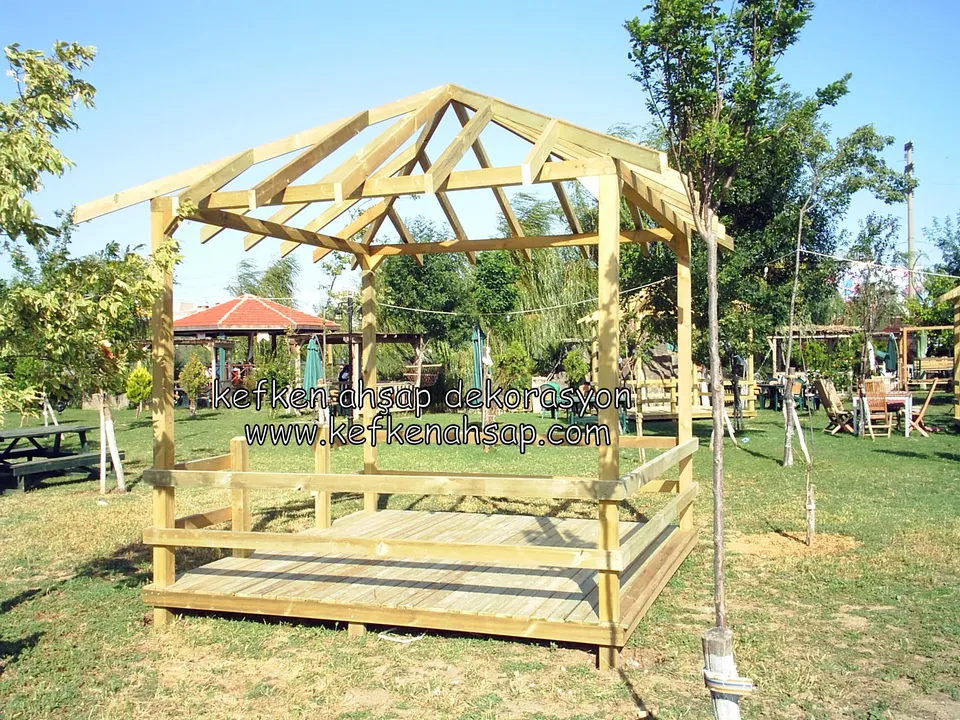 Parkta kamelya iskeleti ve korkuluklu deck, çevrede piknik masaları ve çimlik, arkada bir kamelya daha