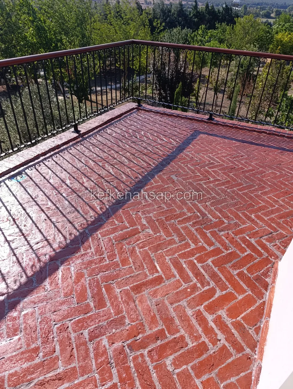 Glossy, freshly sealed red brick terrace floor with a black iron railing and a timber handrail around it