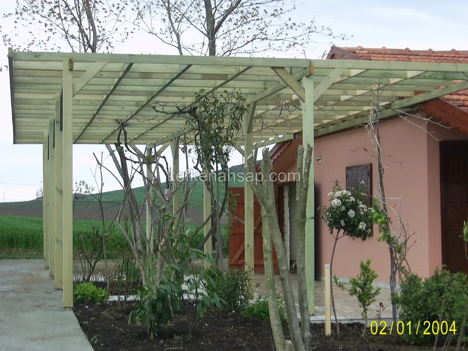 Pembe bahçe evinin önünde uzun, düz çatılı açık yeşil ahşap pergola, önünde güller ve sarmaşık