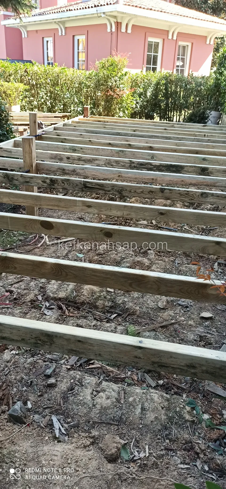 Bahçede pembe binanın önünde sıra sıra dizilmiş yatay deck alt kirişleri