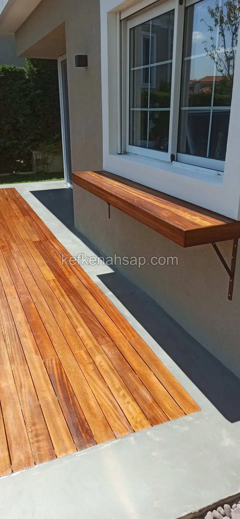 Pencerenin altında metal konsollara oturan ahşap raf ve önünde parlak ahşap deck